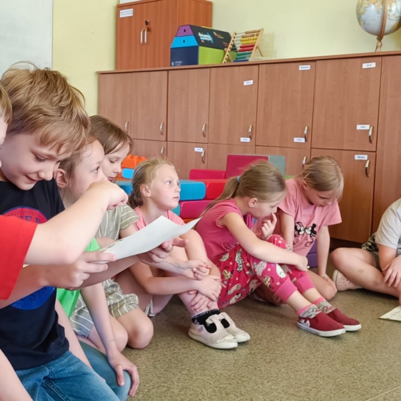 Uczniowie klasy 2 siedzą na podłodze w trakcie spotkania, dwóch chłopców przygląda się kartce