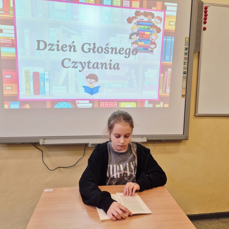 Uczennica klasy 4b czytająca książkę na tle napisu na tablicy