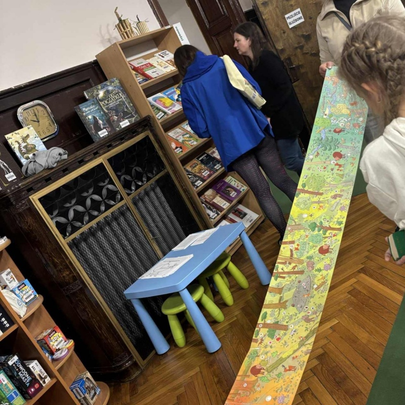 Nauczycielka trzyma długi kolorowy papier/książkę uczennica patrzy