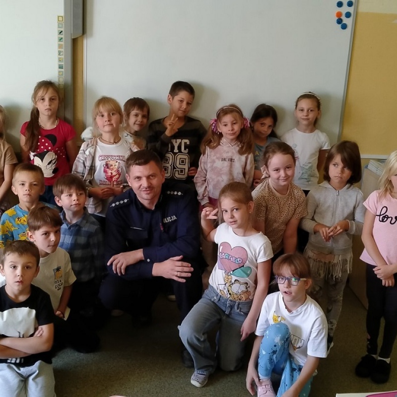 Uczniowie pozują do zdjęcia z policjantem na tle białej tablicy
