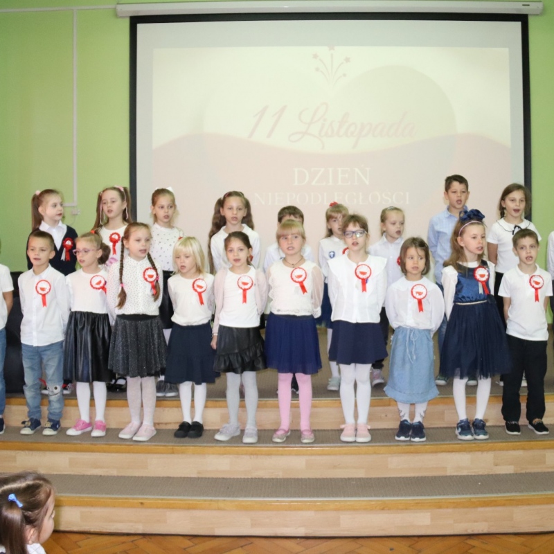 Uczniowie z kotylionami na wyświetlanym tle 11 listopada