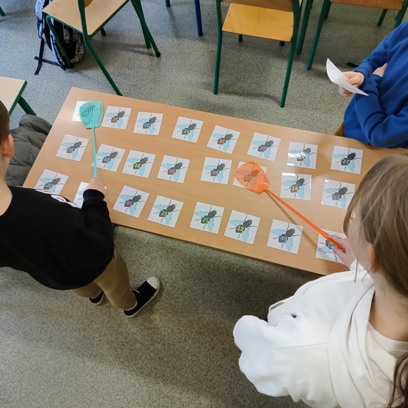 Uczniowie grający w "muchy" - na stoliku obrazki much z liczbami