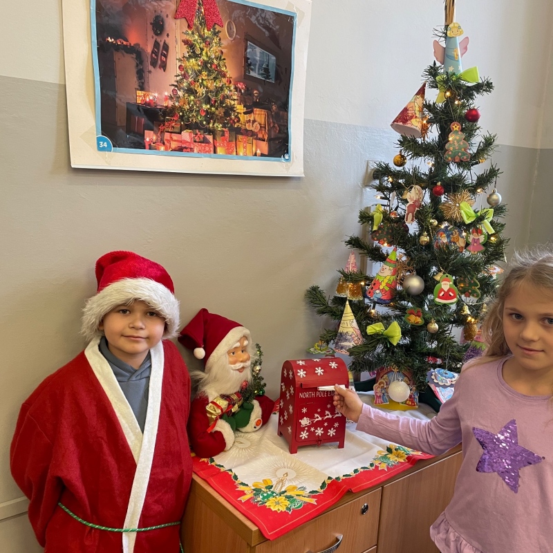 Uczniowie przy skrzynce na listy do Mikołaja w sali i choince jeden uczeń w stroju Mikołaja