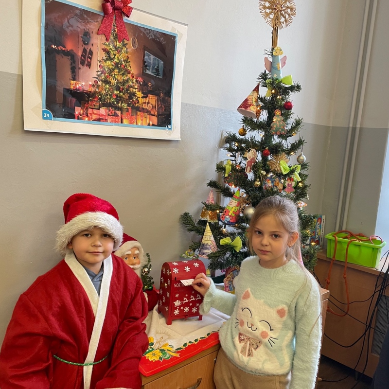 Uczniowie przy skrzynce na listy do Mikołaja w sali i choince jeden uczeń w stroju Mikołaja