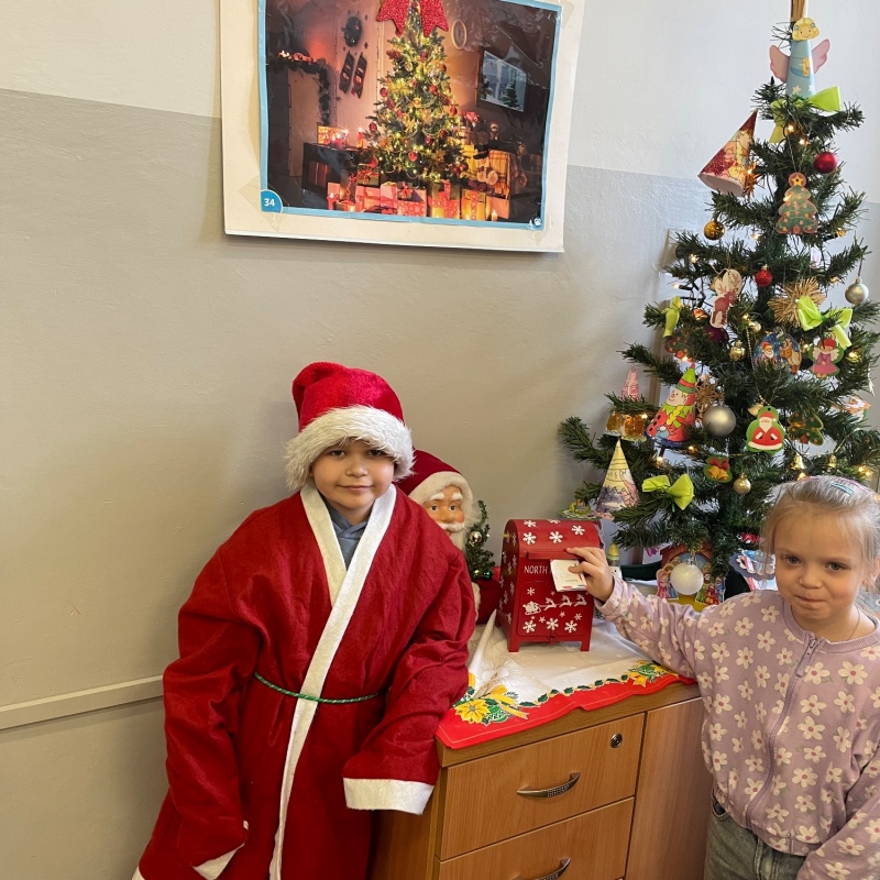 Uczniowie przy skrzynce na listy do Mikołaja w sali i choince jeden uczeń w stroju Mikołaja
