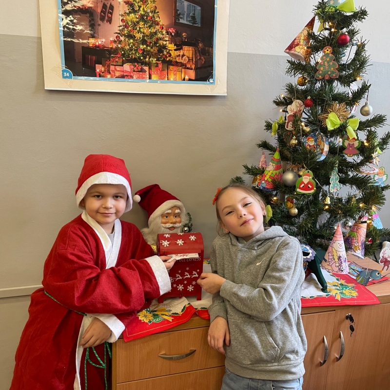 Uczniowie przy skrzynce na listy do Mikołaja w sali i choince jeden uczeń w stroju Mikołaja