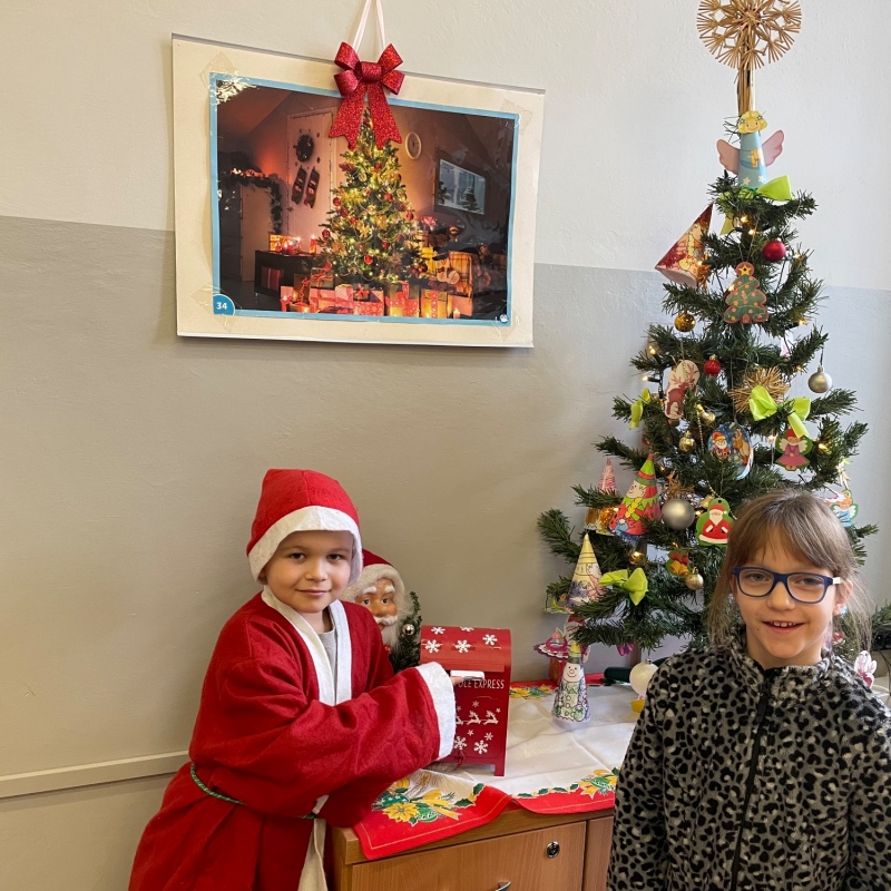 Uczniowie przy skrzynce na listy do Mikołaja w sali i choince jeden uczeń w stroju Mikołaja