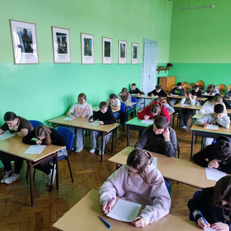 uczniowie w szkolnej auli piszący pracę konkursową