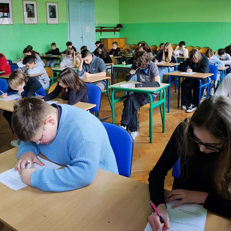 uczniowie w szkolnej auli piszący pracę konkursową