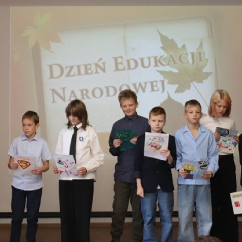 uczniowie w eleganckich strojach na scenie na tle napisu Dzień Edukacji Narodowej