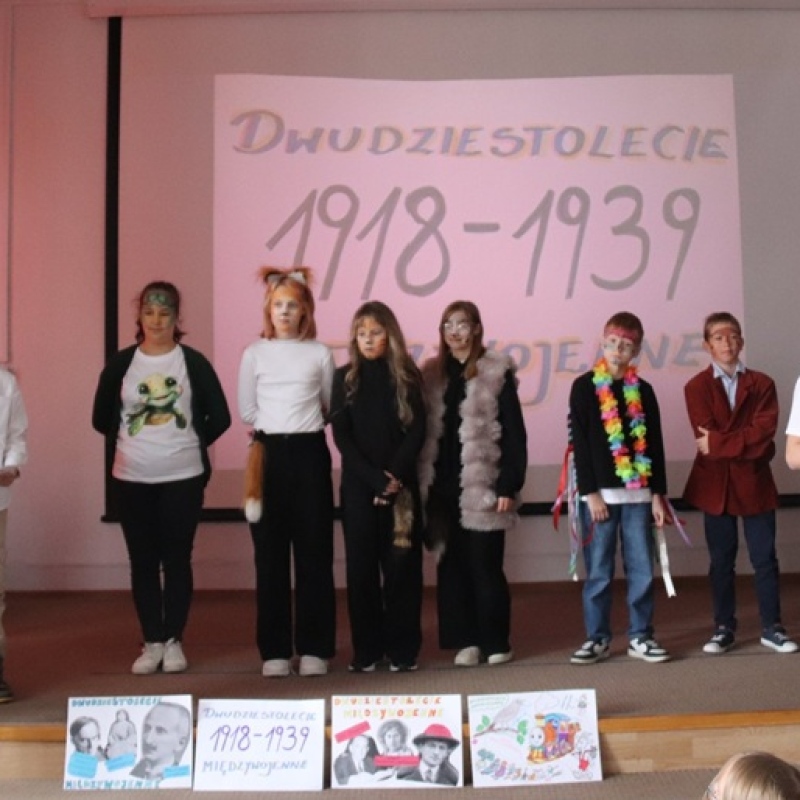 uczniowie na scenie na tle napisu dwudziestolecie międzywojenne